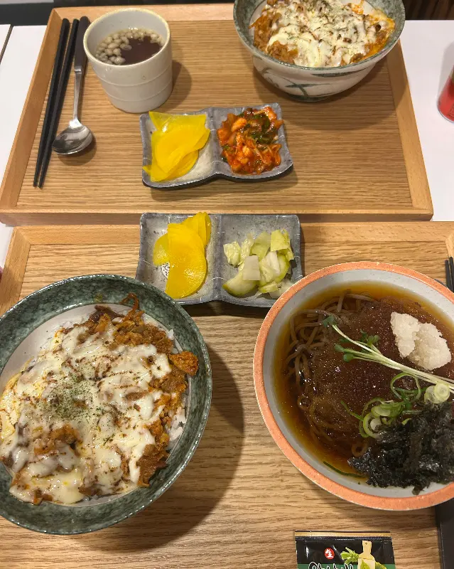 두 개의 나무 쟁반 위에 각각 다른 메뉴가 놓여져 있다. 김치치즈규동, 냉모밀, 규동, 치즈김치가츠동의 모습