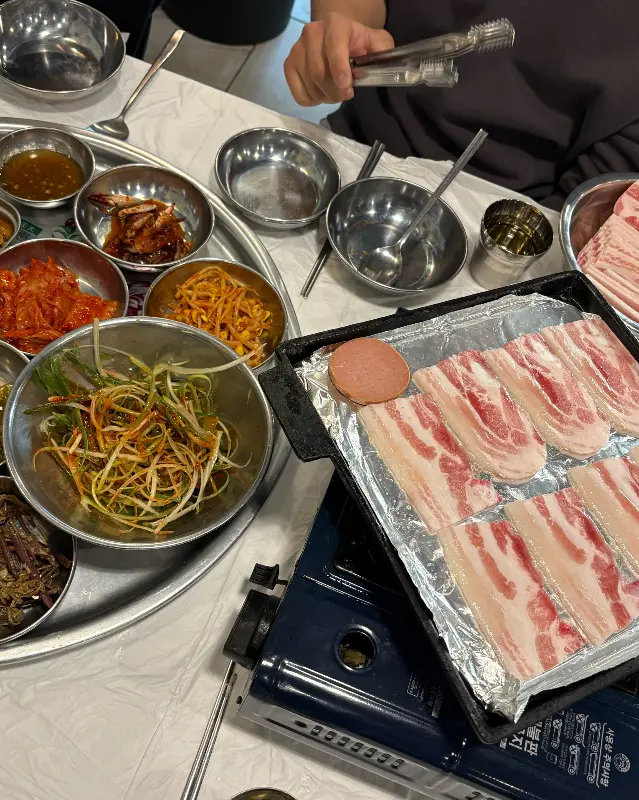 불판 위에 냉동 삼겹살과 다양한 반찬들이 함께 구워지는 모습