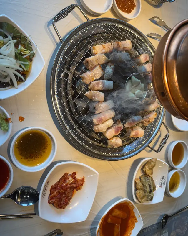 숯불 위에서 다양한 곁들임과 함께 구워지고 있는 고기