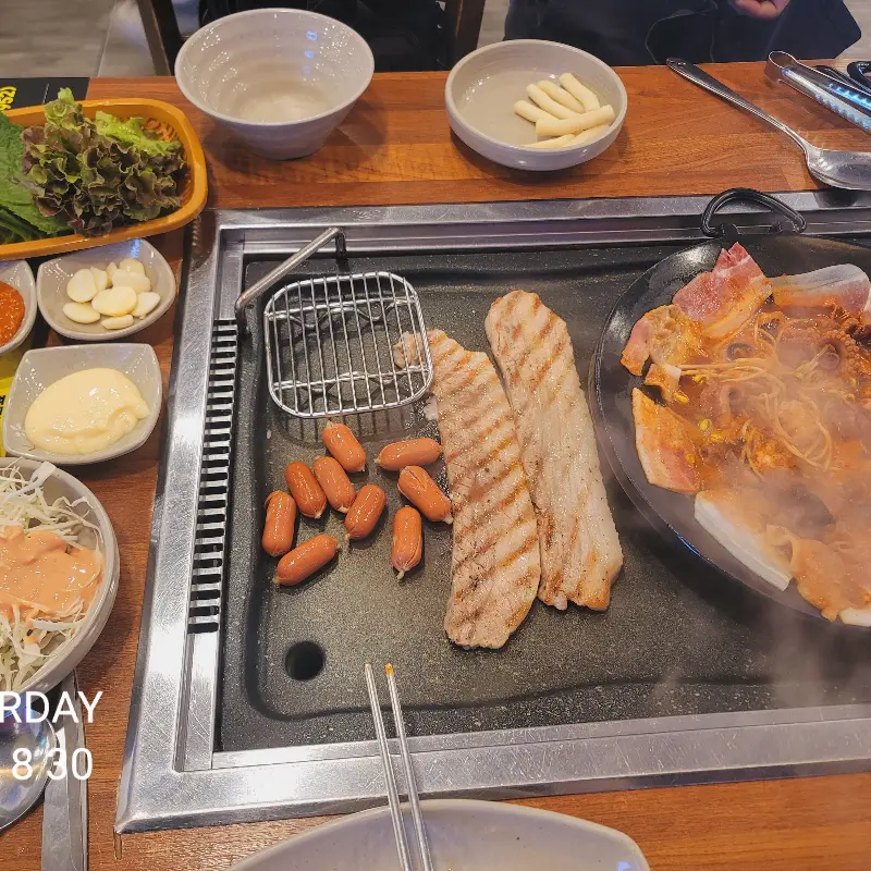 불판 위에 쭈꾸미, 삼겹살, 소세지, 버섯 등이 함께 구워지고 있는 모습