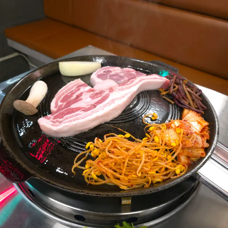 솥뚜껑에 구워진 삼겹살과 김치, 콩나물, 고사리