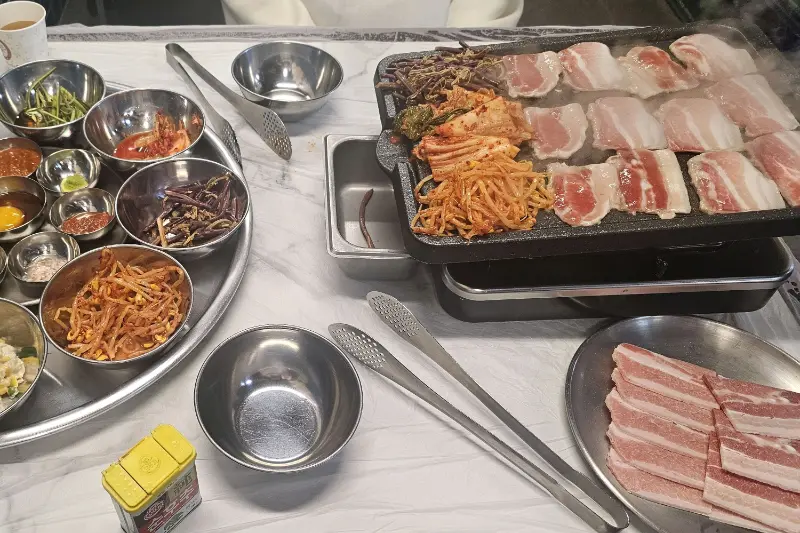 불판 위에 가지런히 놓인 냉삼과 다채로운 반찬들