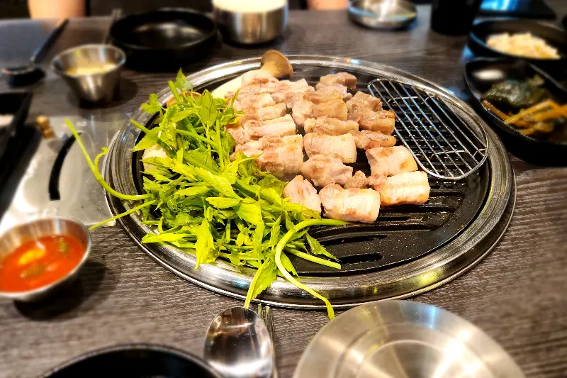 철판 위에 삼겹살과 미나리가 함께 구워지고 있는 모습