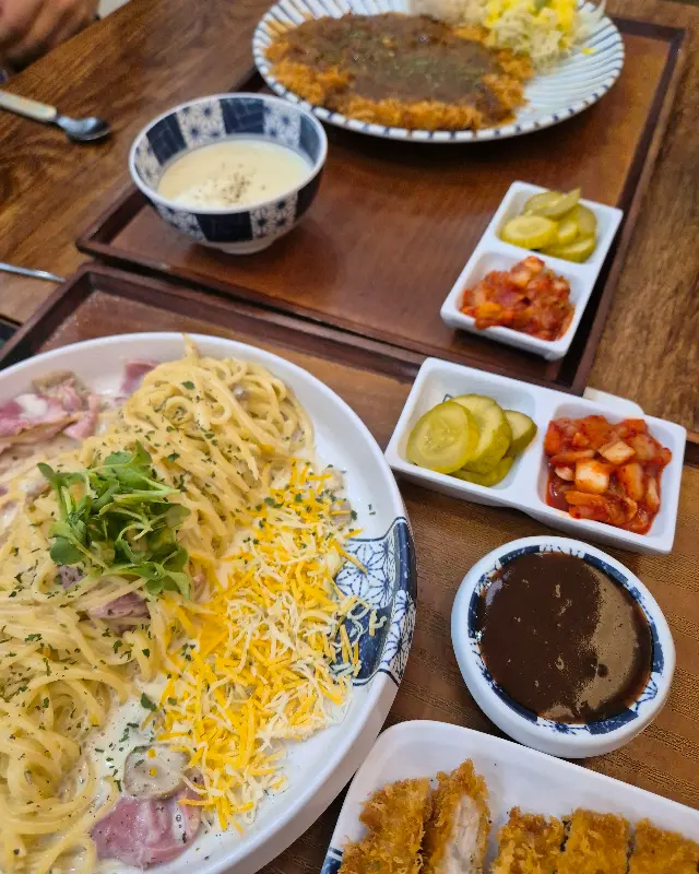 테이블 위에 돈까스, 파스타, 곁들임 메뉴들이 놓여있다.