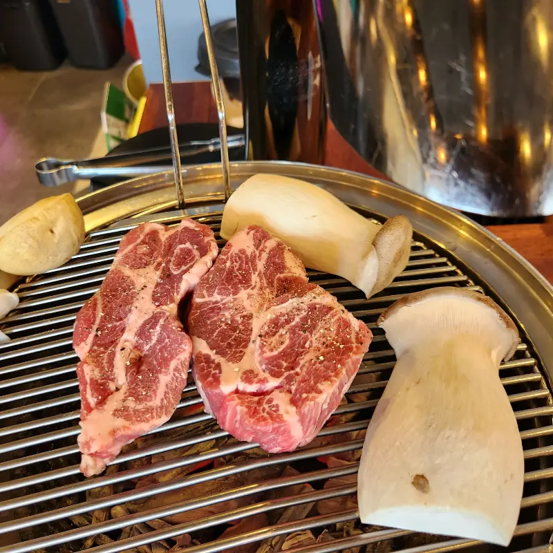 불판 위에서 익어가는 고기와 새송이버섯