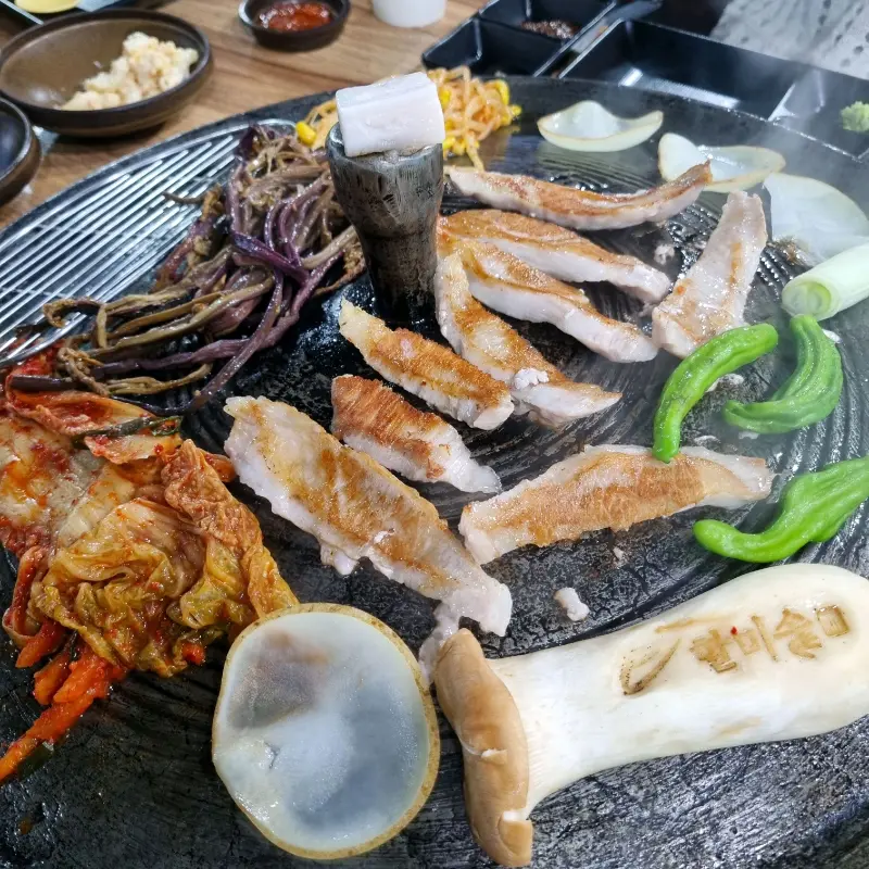 솥뚜껑에 삼겹살, 김치, 콩나물, 고사리 등을 함께 구워 먹는 모습