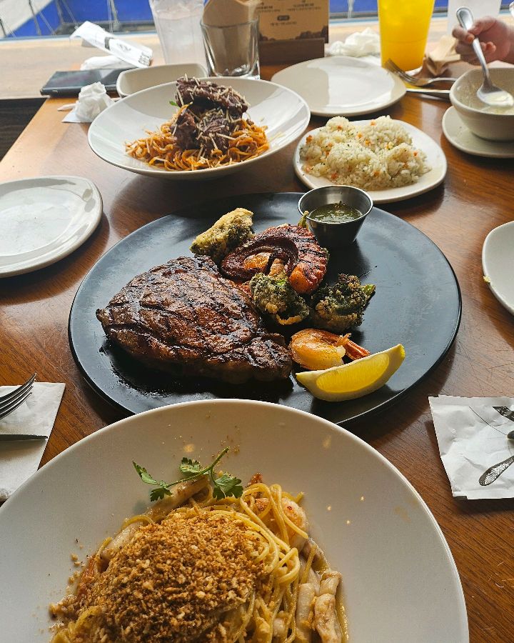 스테이크와 파스타, 볶음밥, 구운 야채 등이 한 상 가득 차려진 모습