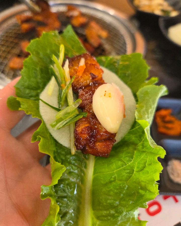 싱싱한 쌈 채소에 양념 불고기와 마늘을 올려 쌈을 싸 먹는 모습