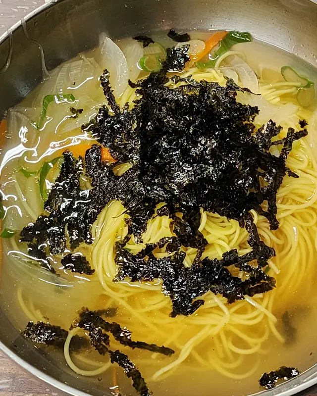 김가루가 듬뿍 뿌려진 멸치 국수가 스테인리스 그릇에 담겨 있는 모습