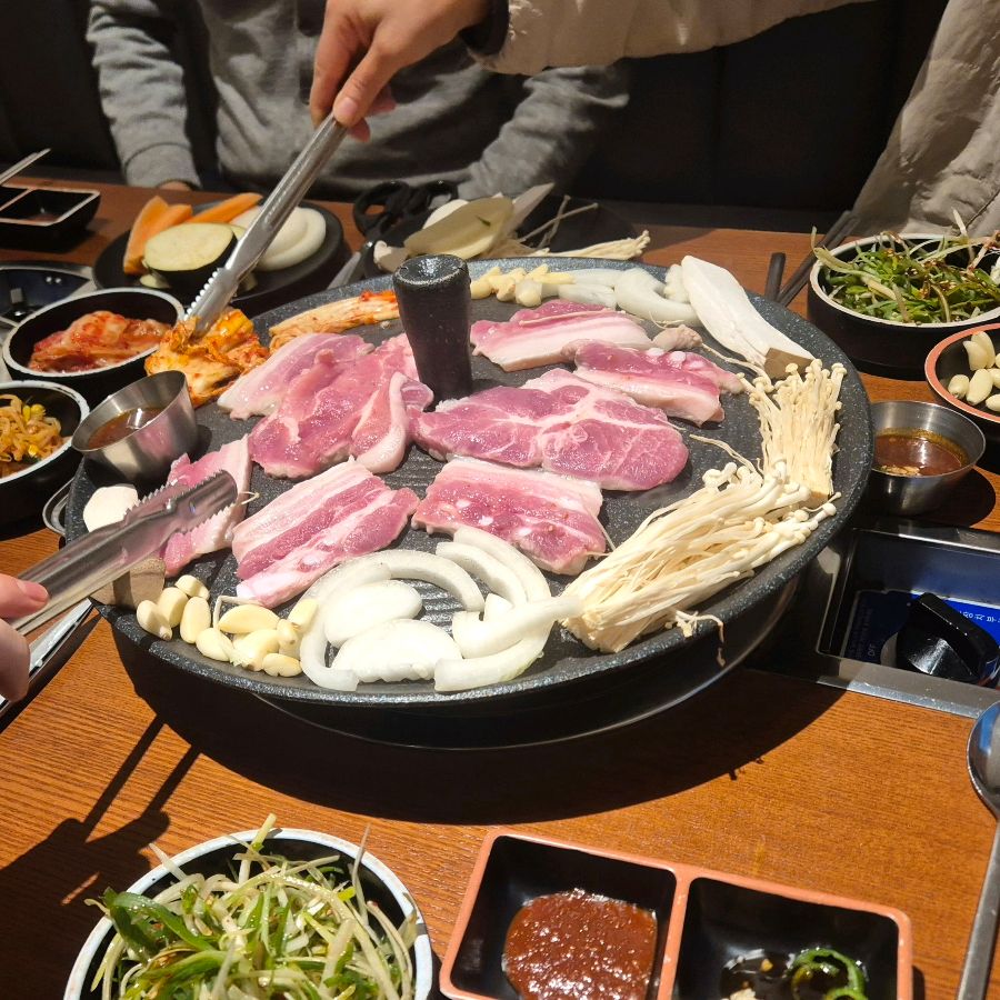 솥뚜껑 불판에 구워지는 삼겹살과 다양한 재료들