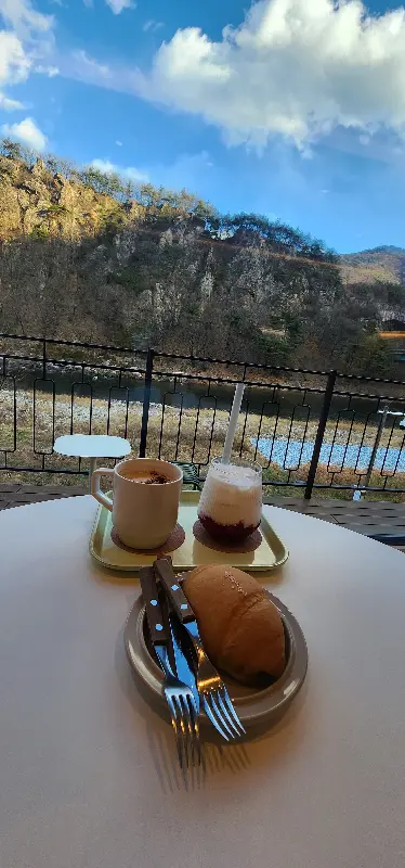 강가 옆 테이블에 놓인 커피와 빵