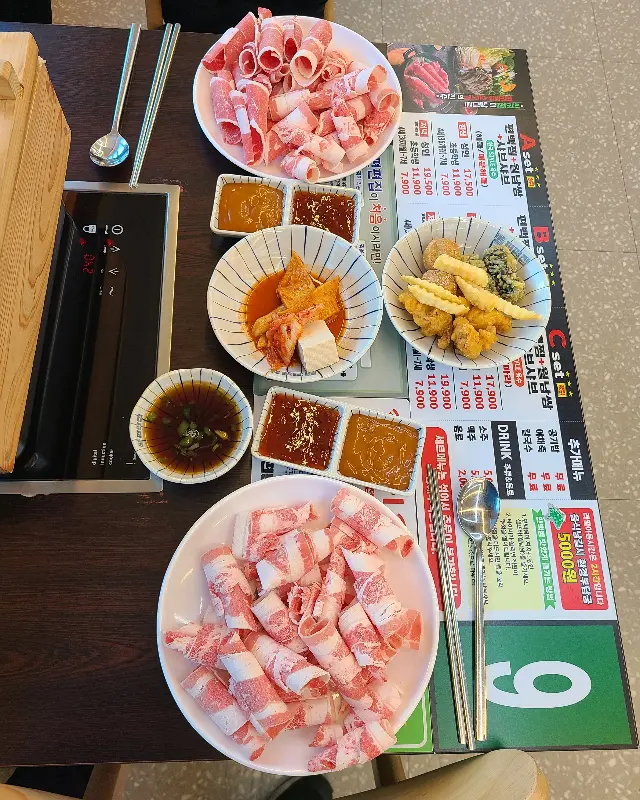 테이블 위에 편백찜과 샤브샤브 재료, 그리고 다양한 소스들이 놓여 있는 모습