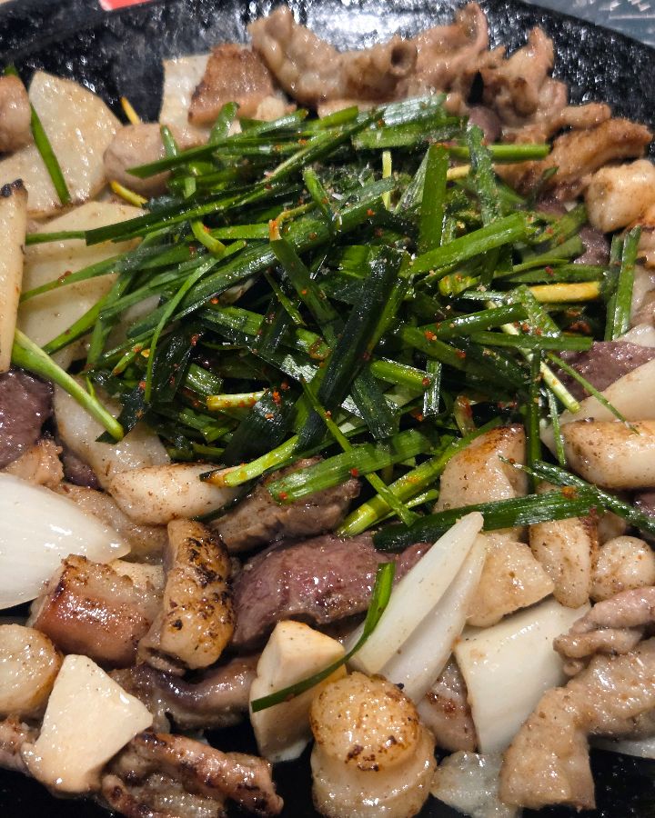 돌판 위에 곱창, 대파, 양파, 감자가 함께 구워지고 있는 모습