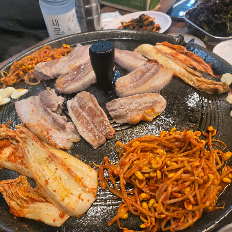 솥뚜껑에 삼겹살과 김치, 콩나물 등이 푸짐하게 구워진 모습