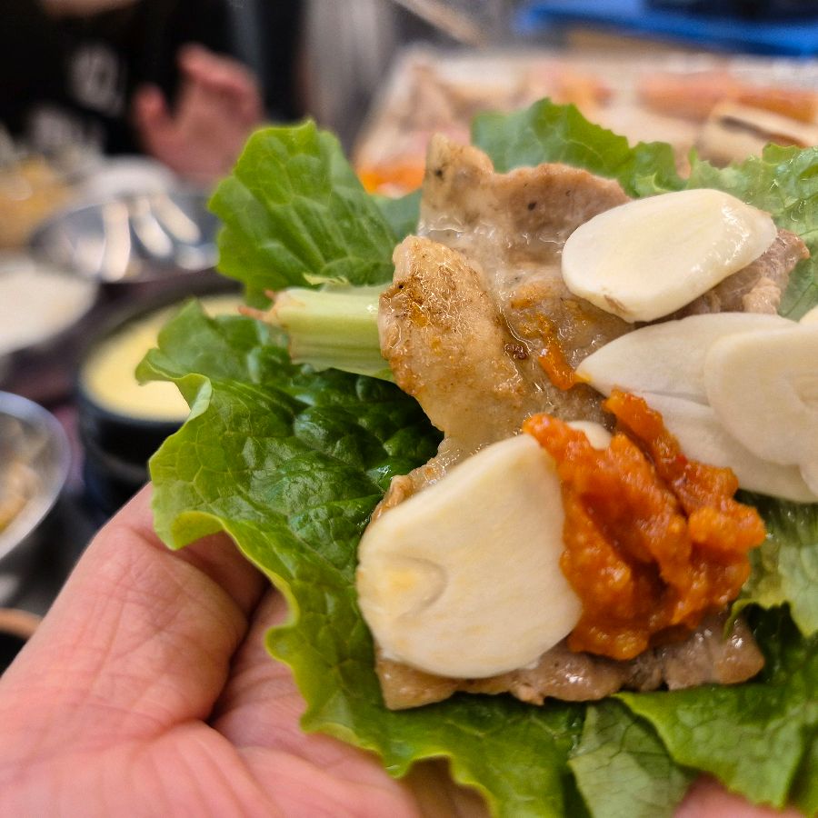 잘 익은 냉삼 한 점을 쌈 채소에 올려 먹는 모습