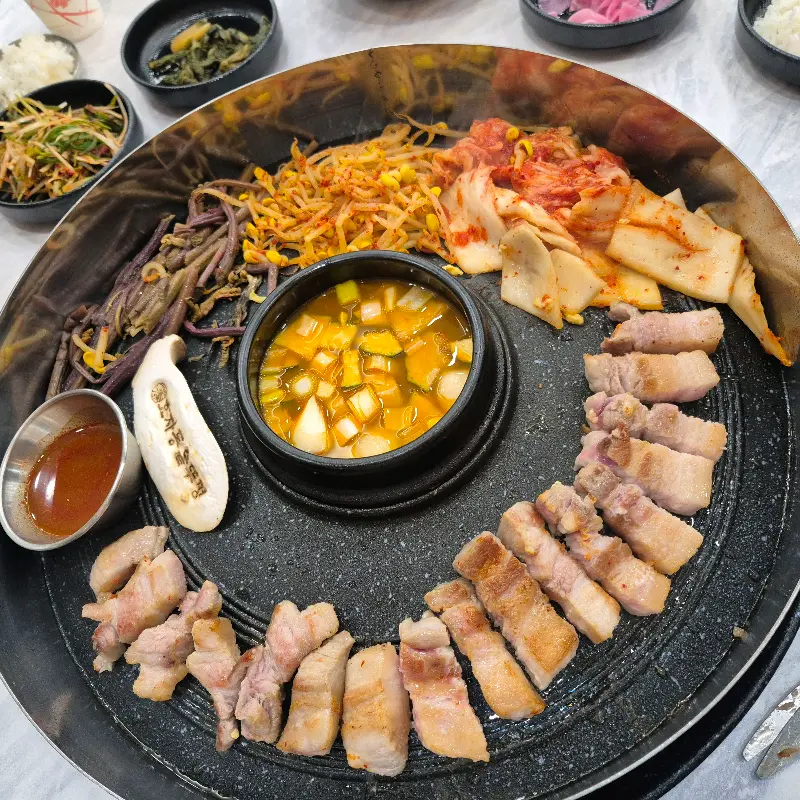 솥뚜껑 위 삼겹살과 반찬 전체샷