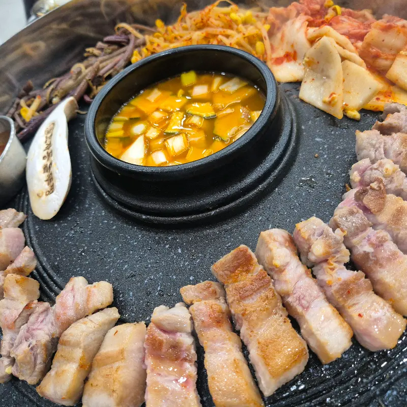 솥뚜껑에 구워지는 삼겹살과 김치, 콩나물, 고사리