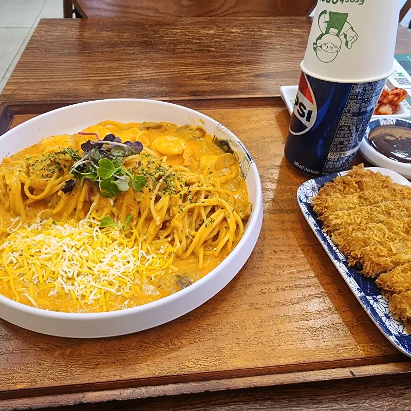 테이블 위에 돈까스와 파스타, 음료가 놓여있다.