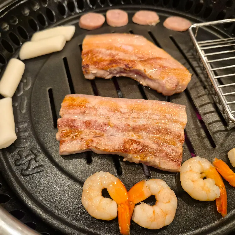 불판 위에서 구워지는 삼겹살, 떡, 새우