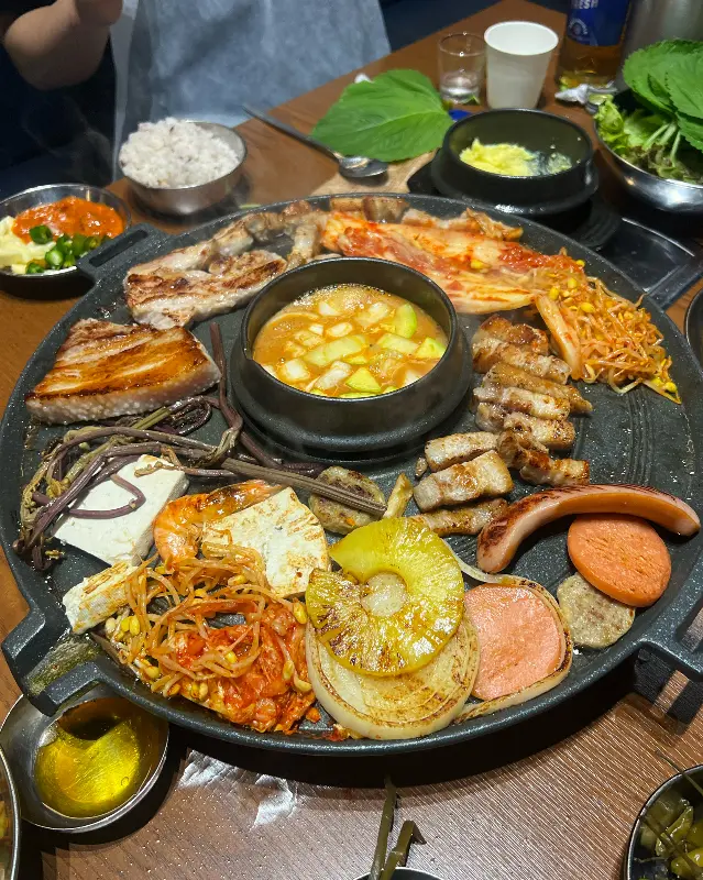 솥뚜껑 한가득 올려진 삼겹살과 각종 구이 재료들