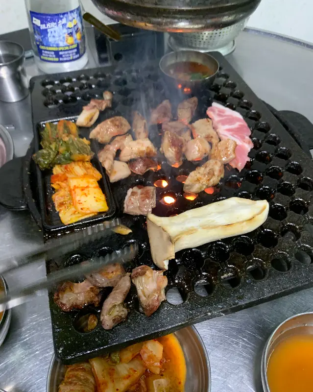 연탄불 위에서 지글거리는 고기와 김치, 버섯