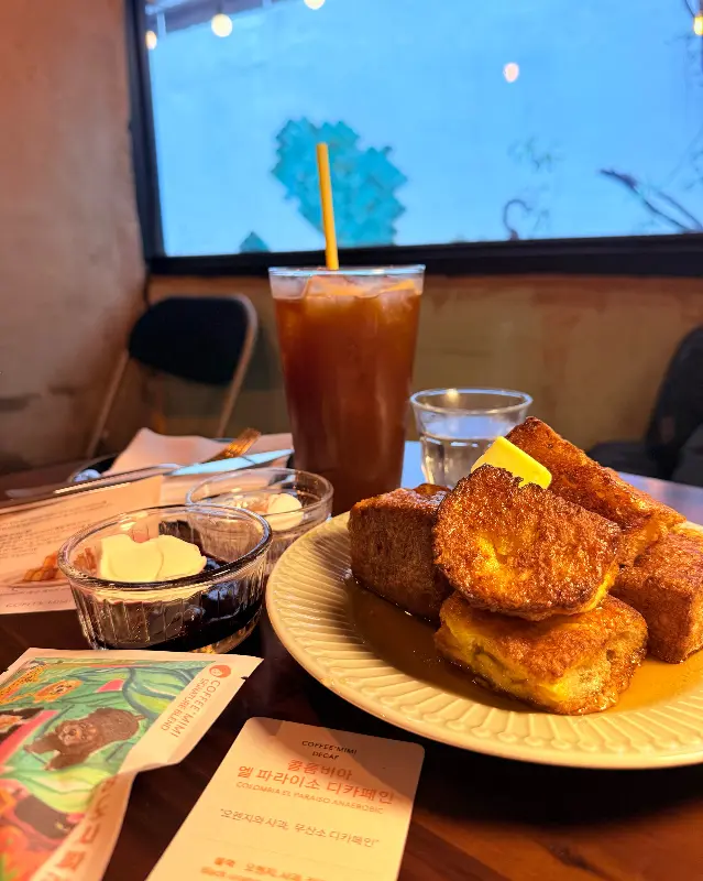 창밖 풍경을 배경으로 놓인 프렌치토스트와 아이스 아메리카노