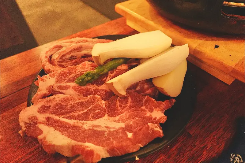 두툼한 고기와 새송이버섯이 접시에 담겨 있다.