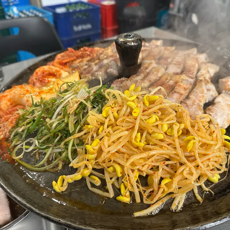 솥뚜껑 가득 채워진 삼겹살과 다양한 곁들임