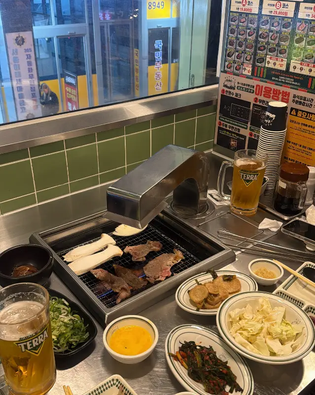 테이블 위 화로에서 구워지는 고기와 맥주