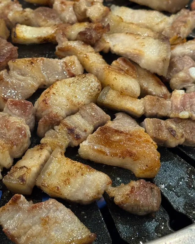 불판 위에서 노릇하게 익어가는 흑돼지 오겹살