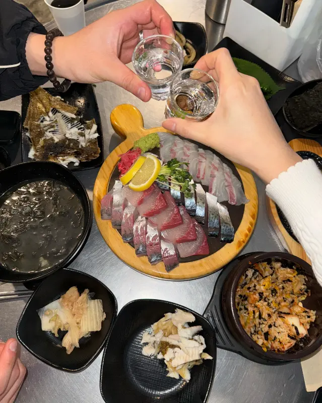 테이블 위에 놓인 회와 술잔을 들고 건배하는 모습