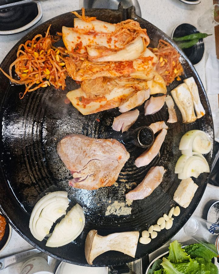 솥뚜껑에 구워지는 삼겹살, 김치, 콩나물