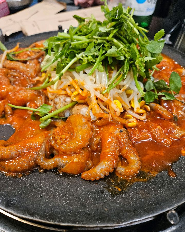 매콤한 양념에 버무려진 쭈꾸미 위에 아삭한 콩나물과 미나리가 듬뿍 올려진 모습