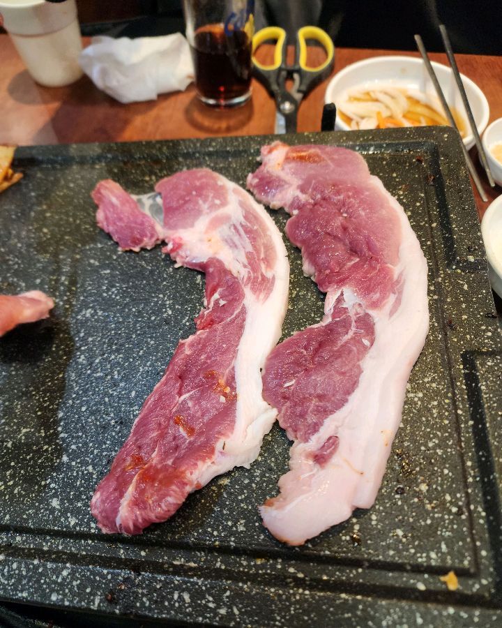 불판 위에 올려진 두툼한 삼겹살. 선명한 붉은 색이 신선함을 더합니다.