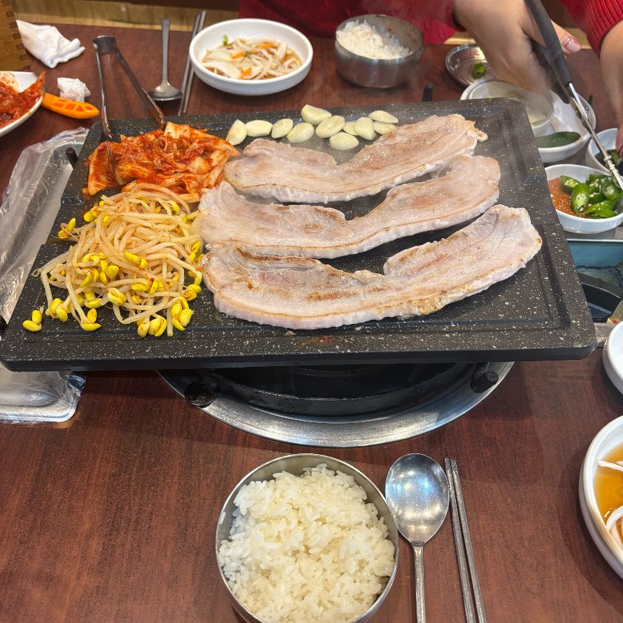 삼겹살, 김치, 콩나물, 마늘까지 푸짐하게 불판 위에 올려 굽는 모습.