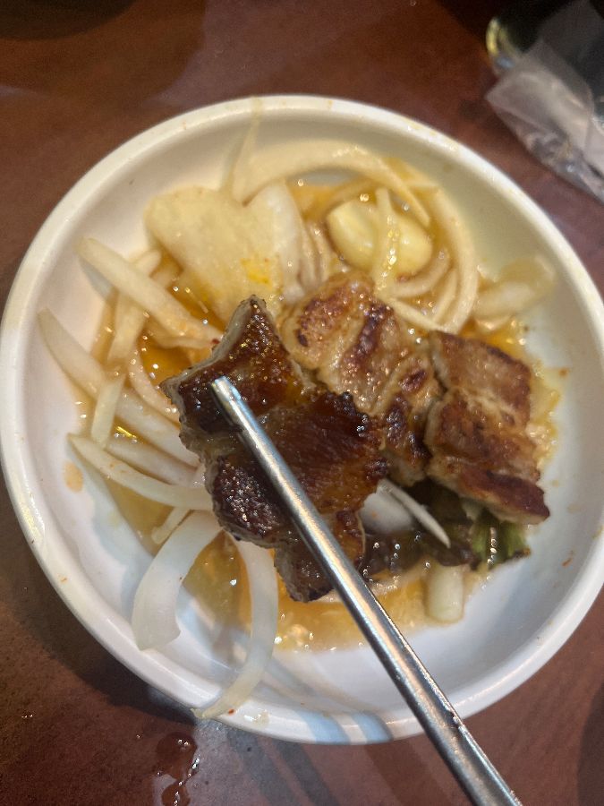 잘 구워진 삼겹살 한 점을 특제 소스에 찍어 먹는 모습.