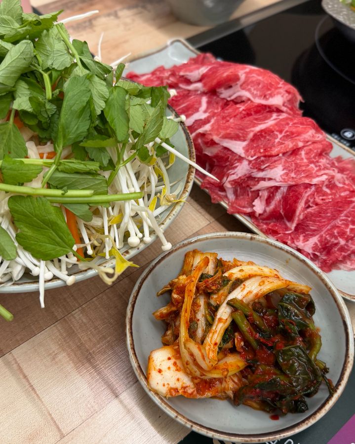 싱싱한 채소와 얇게 썰린 소고기, 그리고 잘 익은 김치가 조화롭게 놓여있는 모습