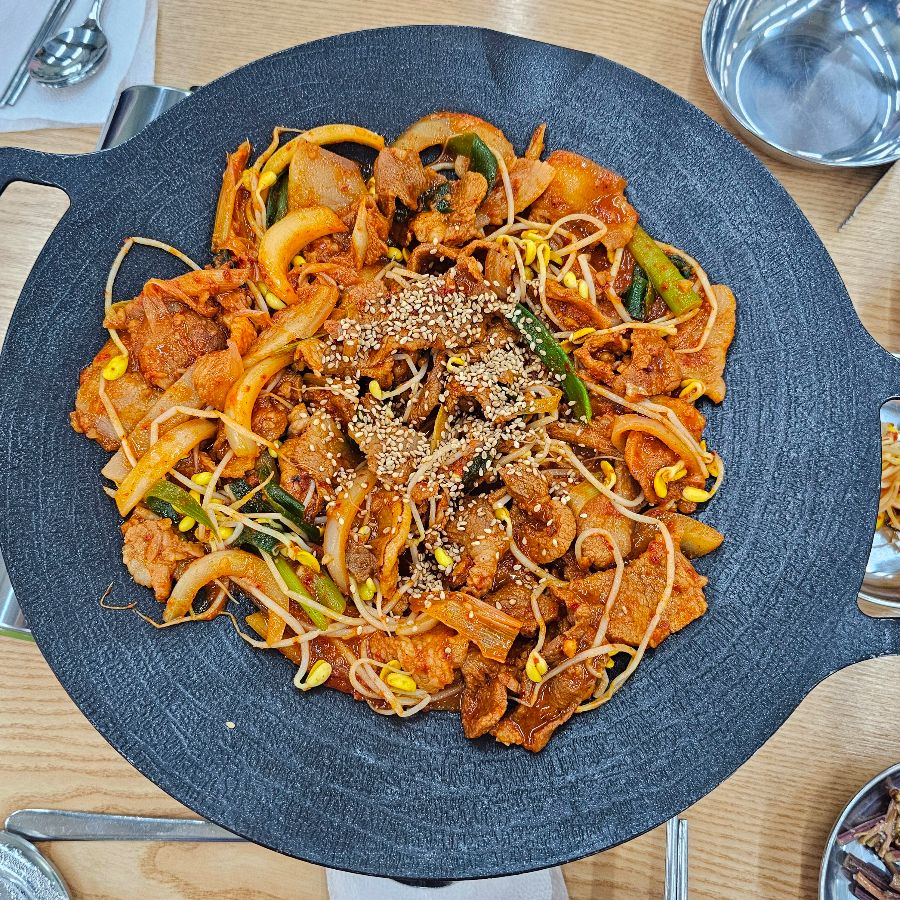 뜨겁게 달궈진 철판 위에 놓인 신비육돈의 제육볶음. 윤기가 흐르고 깨가 듬뿍 뿌려져 있어 먹음직스럽다.