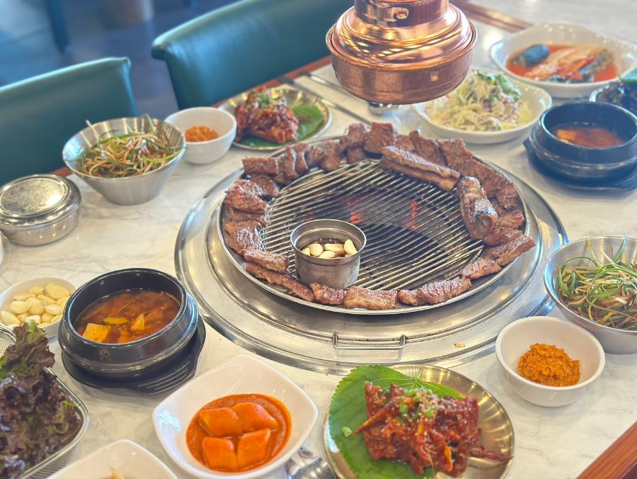 숯불 위에 가지런히 놓인 돼지 왕갈비와 정갈한 곁들임 음식들이 풍성한 식탁을 채우고 있는 모습