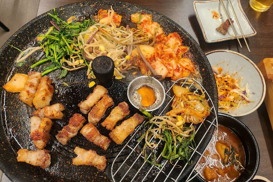 불판 위에서 익어가는 삼겹살, 김치, 콩나물의 조화