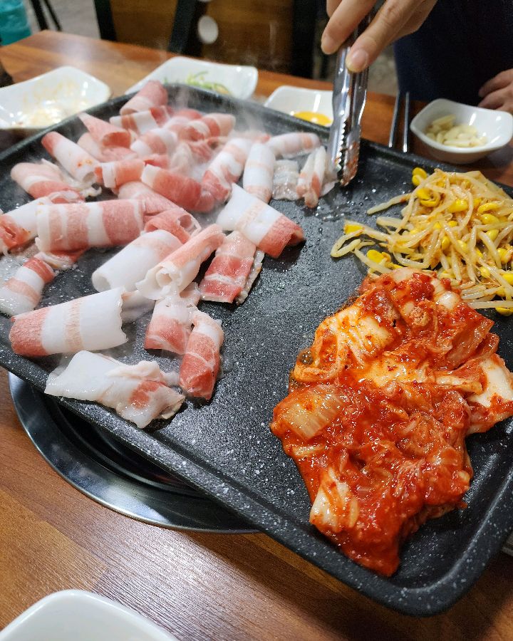 대패삼겹살과 김치, 콩나물무침이 함께 구워지는 모습