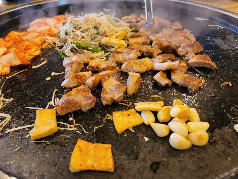 잘 익은 삼겹살과 김치, 콩나물, 마늘 등이 철판 위에서 조화를 이루는 모습