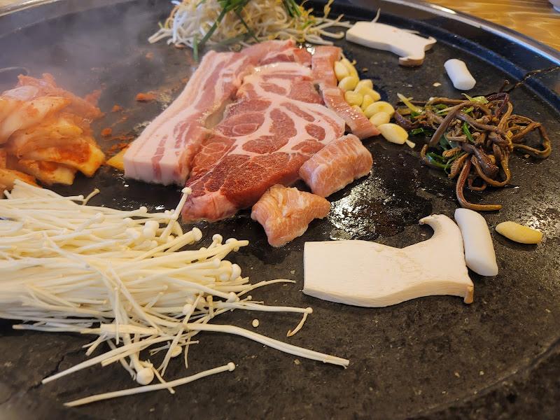 삼겹살과 함께 김치, 버섯, 콩나물 등이 철판 위에 푸짐하게 올려져 있는 모습