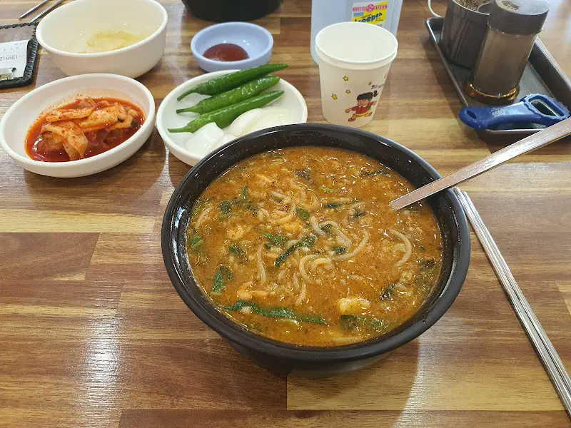 추어탕이 담긴 검은색 뚝배기와 반찬 그릇들이 나무 테이블 위에 놓여있는 모습