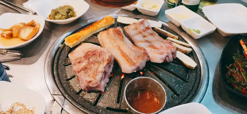 흑돼지 오겹살, 목살, 멜젓, 밑반찬이 함께 차려진 모습