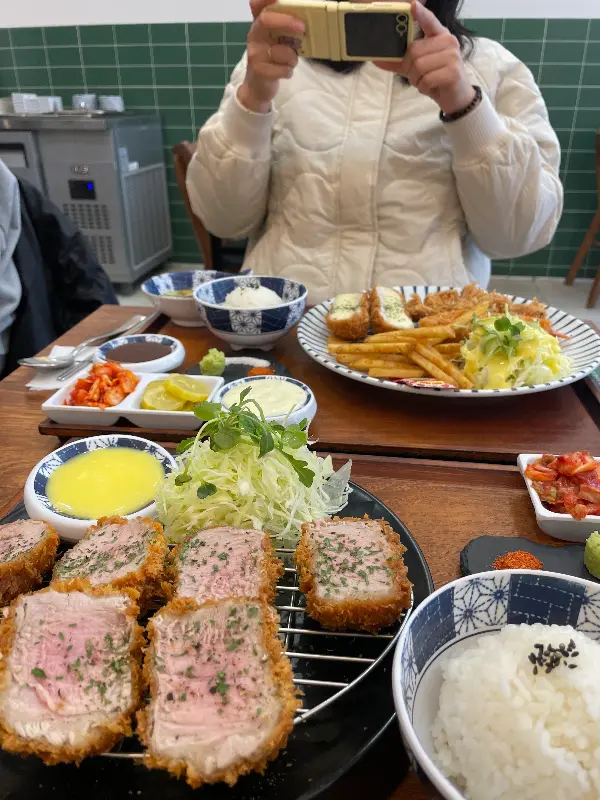 테이블 위에 돈까스와 감자튀김, 샐러드가 놓여있다.