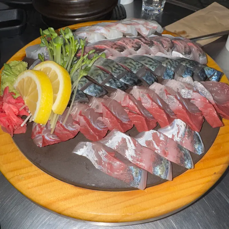 신선한 고등어회와 대방어회가 나무 도마 위에 정갈하게 담겨 있는 모습