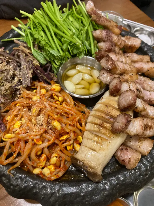 돌판 위에 가득한 삼겹살과 곁들임 채소들