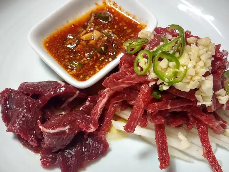 잘게 썰린 육회 위에 다진 마늘과 고추가 얹어져 있고, 옆에는 양념장이 놓여 있다.