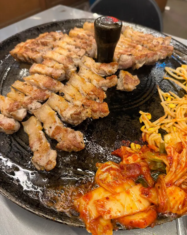 솥뚜껑에 구워진 삼겹살과 김치, 콩나물의 모습